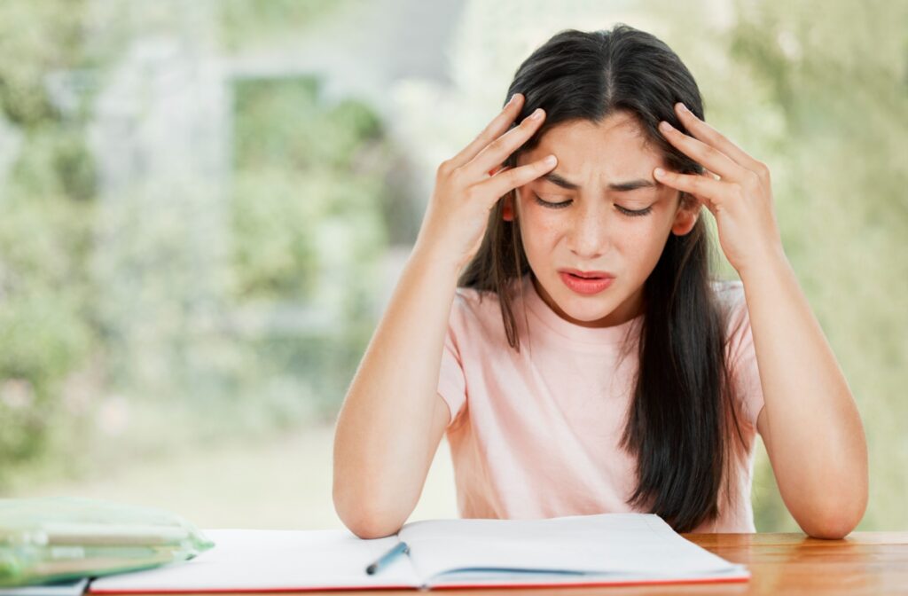 A young girl looks distressed because she is struggling to read due to vision problems.