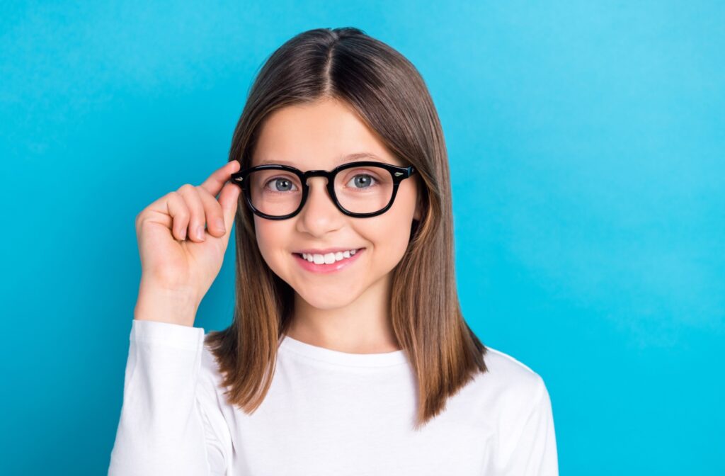 A young child adjusting their new glasses for myopia control in front of a blue background.