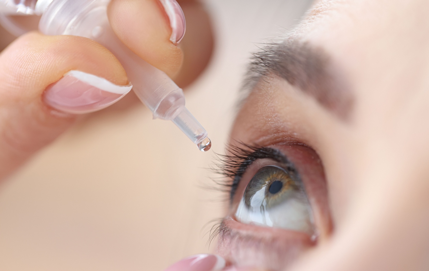 A person uses their hand to squeeze prescription eye drops into their eye for dry eye relief.
