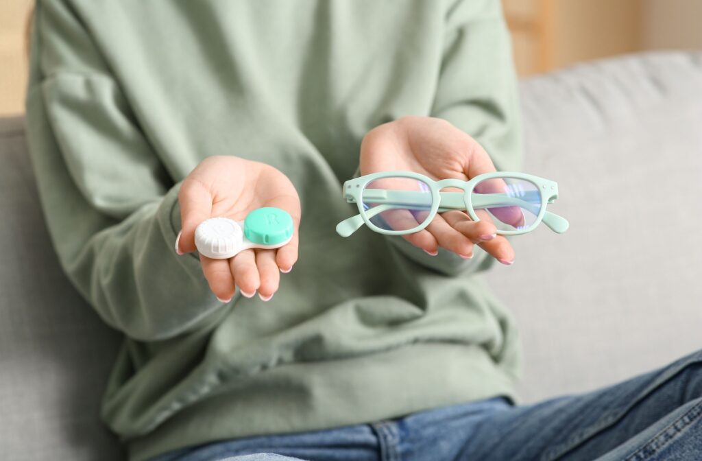 A person holding up a contact lens case and a pair of glasses in each hand.