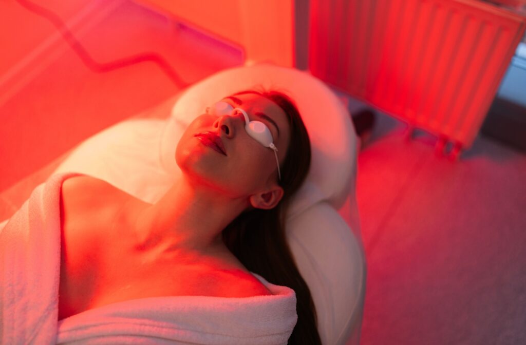A person laying down wearing eye protection while receiving red light therapy.